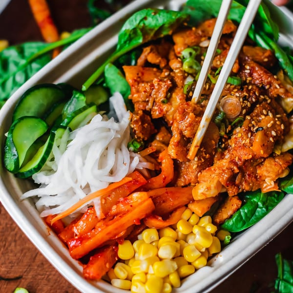 Matko's Korean spicy pork bowl with spinach, cucumbers, kimchi, corn, and chopsticks.
