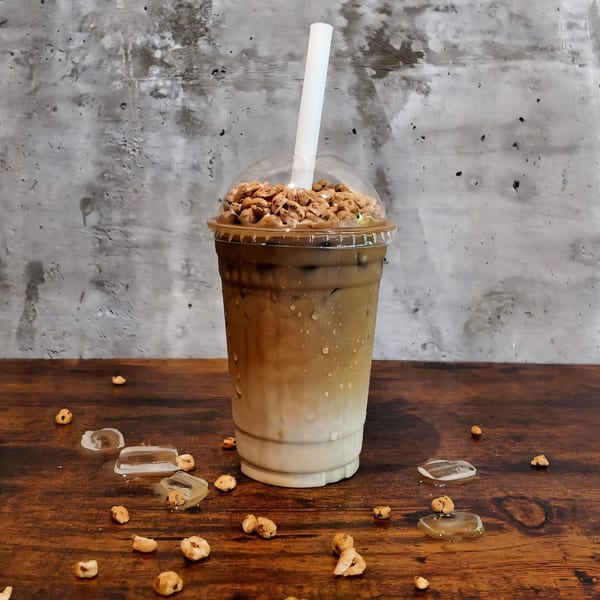 Iced coffee with a layer of milk, topped with crunchy cereal, on a wooden table.