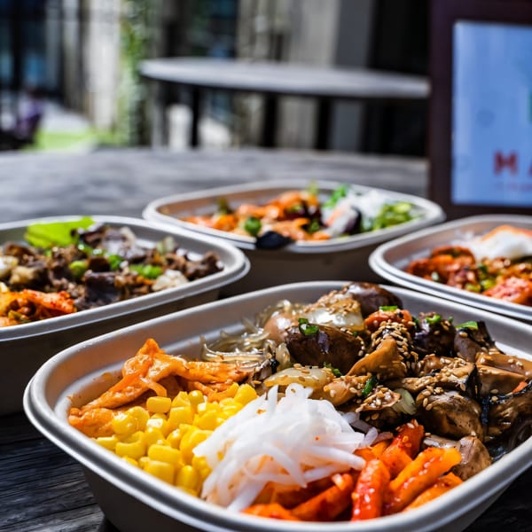 Four Matko Korean bowls with various toppings, including mushrooms, corn, and kimchi, on a wooden table.