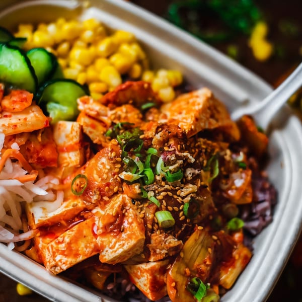 Close-up of a Matko Korean bowl with tofu, kimchi, corn, and cucumbers in a white container.